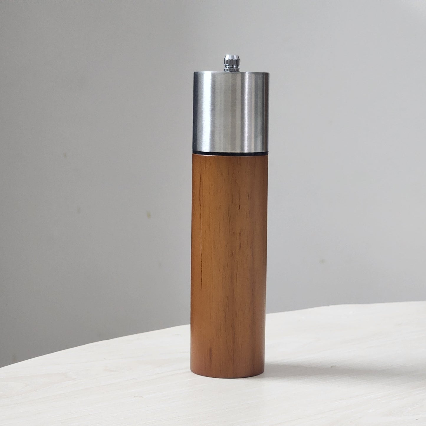 Wooden pepper grinder with metal top on a white surface and gray background