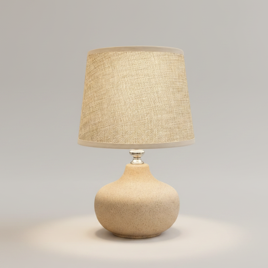 A table lamp with a textured beige fabric drum shade and a matching speckled beige ceramic base, shown against a neutral light gray background.